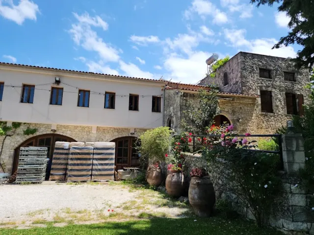Stone and plaster buildings around a yard, large clay jars with flowers and stacked barrels