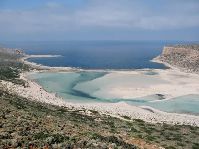 A shallow pale blue lagoon between a white sand spit and a rocky hill