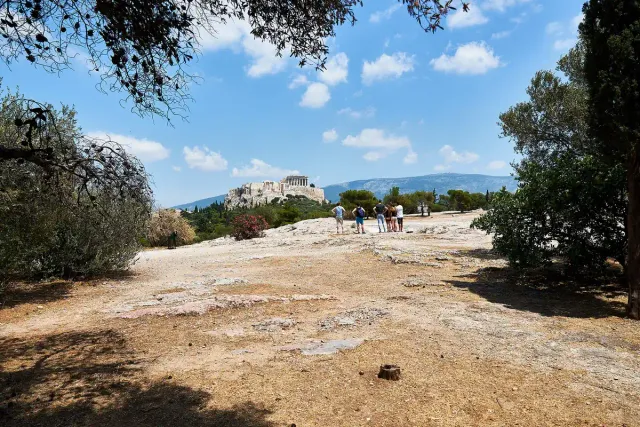 A dusty rocky slope with walkers, the Acropolis hill in the distance