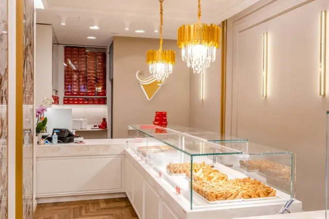 A glass display case with triangular pastries, golden chandeliers and red boxes on the shelves
