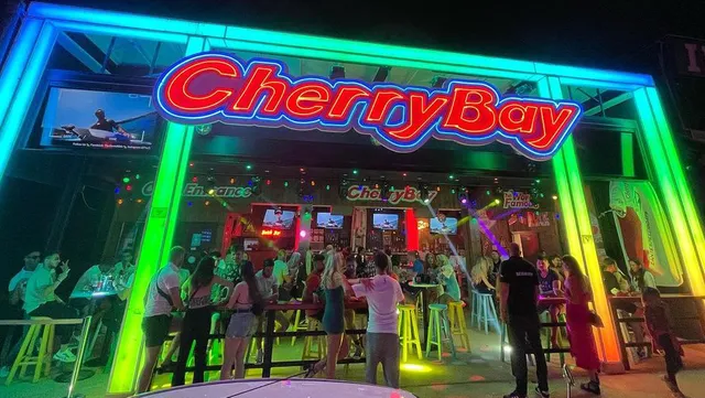A large red neon sign above an open bar, with people standing in colourful lighting