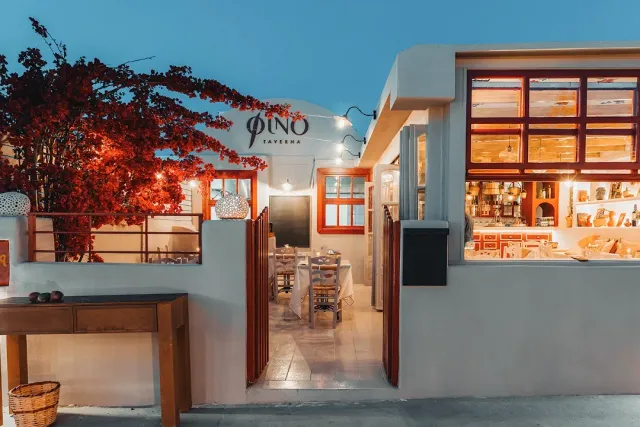 A whitewashed front lit in the evening, an entrance to a seating courtyard and red blossom