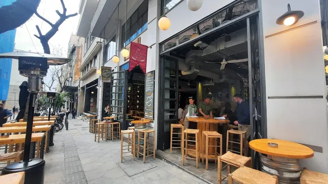 A bar front open to the street with wooden stools, barrels as tables and heaters on the pavement