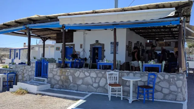 A white building with a reed canopy and blue chairs, above a stone wall