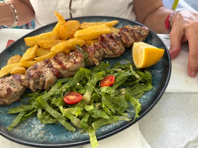 A grilled meat skewer with fries, shredded lettuce and a lemon wedge on a blue plate