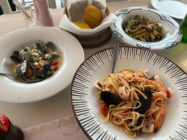 Plates of seafood pasta and mussels in sauce, beside a bread basket on a table