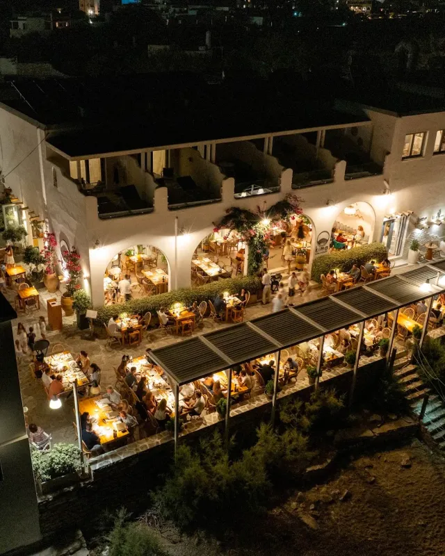 A night aerial view of a lit white building with arches and terraces full of diners