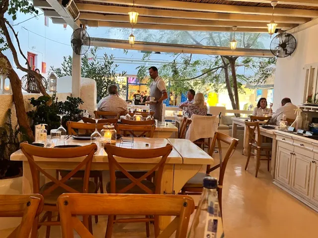A covered terrace with wooden beams, hanging lamps and tables with diners seated around them