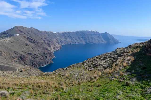 A green slope on the caldera rim, with steep cliffs dropping to deep blue sea