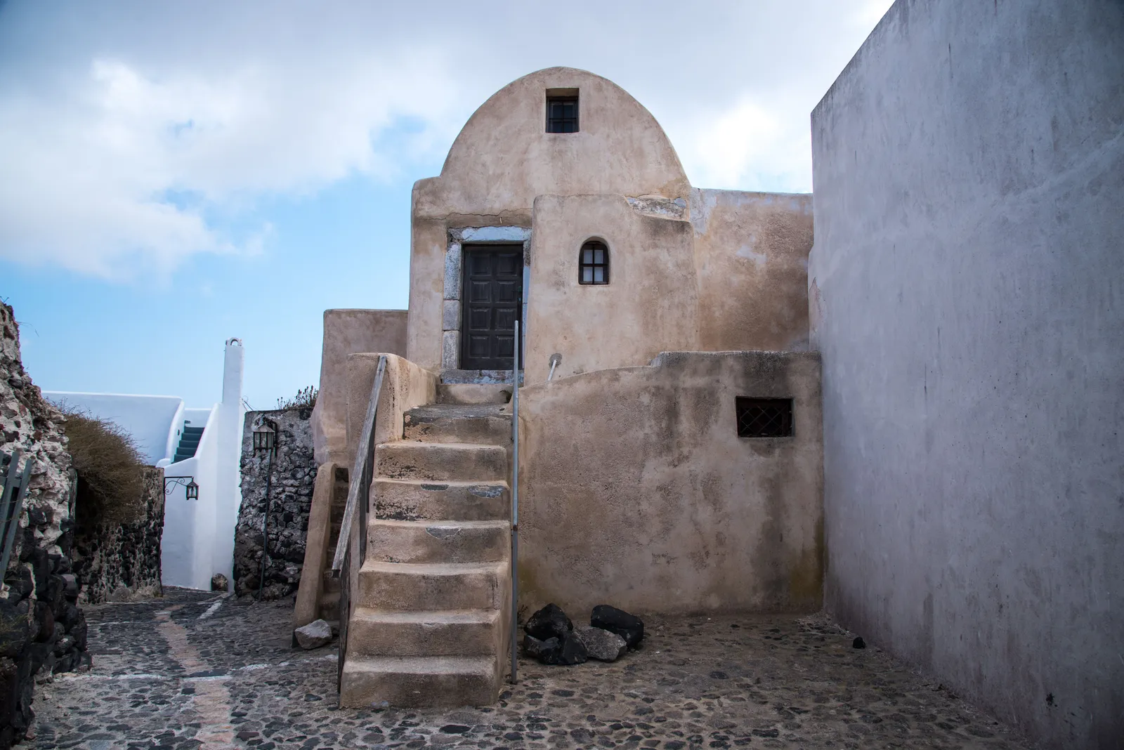 A traditional stone house with an external staircase and a domed roof in a Cycladic village
